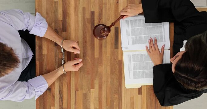 Man in handcuffs and judge sit at table with a gavel and documents