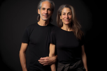 A professional photo of an attractive middle-aged couple wearing black t-shirts, posing for a portrait studio photoshoot in front of a solid dark background.