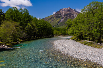 Clear, fast flowing river leading through a forest to towering mountain peaks (Hotaka, Matsumoto, Nagano)