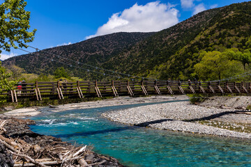Hiking trails and a wooden suspension bridge over a clear fast flowing river and forest (Kamikochi, Japan)