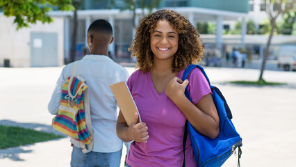 Funny hispanic female student with backpack and paperwork infront of university