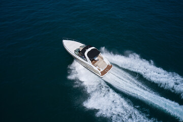 A large white motor boat moves quickly on dark blue water, top view. A white boat moves on the...