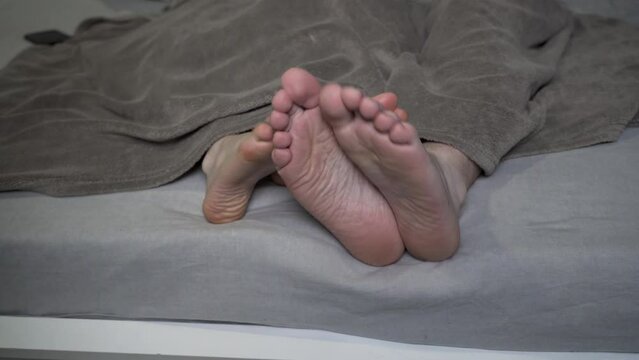 Male and female feet are touching under blanket in bed, couple girl and guy are lying together on the bed linen in a cozy bedroom. Relationship, youth and apartment concept.