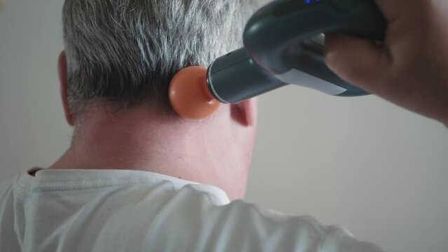 Massage percussion gun at work. Senior man massaging his neck, close-up.