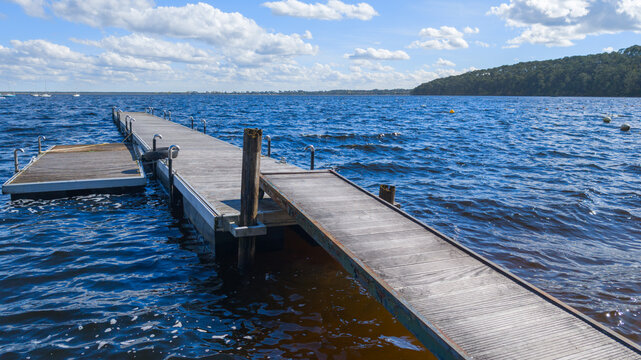 Empty wooden steel pontoon pier over blue carcans lake with clear cloud sky background at day time