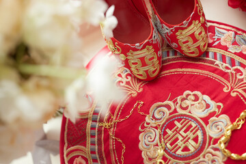 A pair of red and gold embroidered shoes rests on matching fabric, adorned with intricate patterns