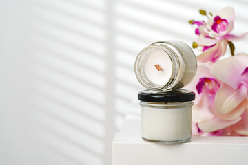 Opened Scented Candle Jar on a White Stand Near a Blurry Orchid Flower
