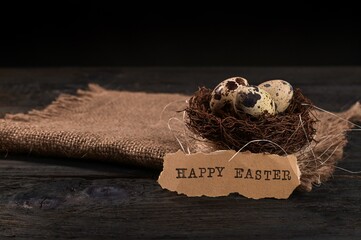 easter quail eggs on burlap on a black wooden background. with the inscription happy Easter.
