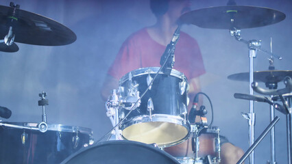 A passionate drummer immersed in a foggy atmosphere creates a mystical musical experience. Drummer on stage in white smoke.