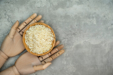 A wooden bowl of rice grains is held by mannequin hands, isolated on grey marble background. A...