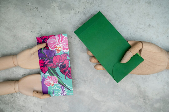 Malay version of money packets known as "Sampul Duit Raya" are held by wooden mannequin hands, isolated on grey marble background. A close-up and selective focus photo of the green money packet.