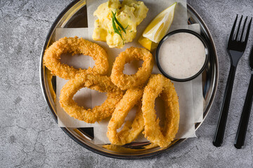 Fried calamari with potato salad next to it on stone table