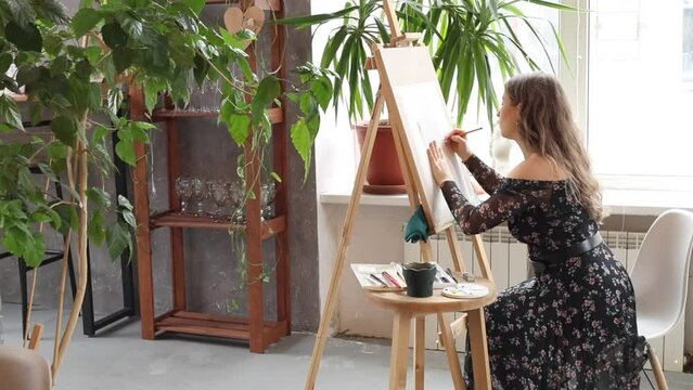 Two women artists painting on big table and wooden easel in art studio. Beautiful girls drawing together in creative loft. Creativity process in craft workshop
