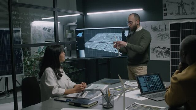 Full medium footage of male alternative energy specialist explaining work of new wind turbine fixing rotor blades to its prototype tower during business conference in office