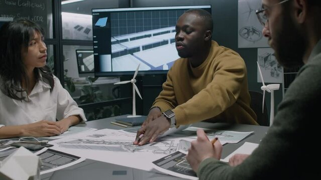 Medium footage of African American team leader pointing out important aspects of redesigning wind turbine nacelle structure for better results in work during meeting, diverse colleagues listening