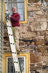 Man climbs ladder leaning against an old stone house for roof repairs carrying a pneumatic brad...