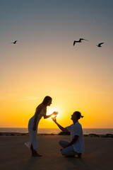 Fototapeta premium Silhouette of a couple during a marriage proposal on the beach with a beautiful sunset backdrop