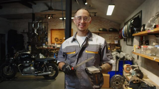 Medium portrait of male technician in googles and uniform holding sharpening stone in motorbike garage