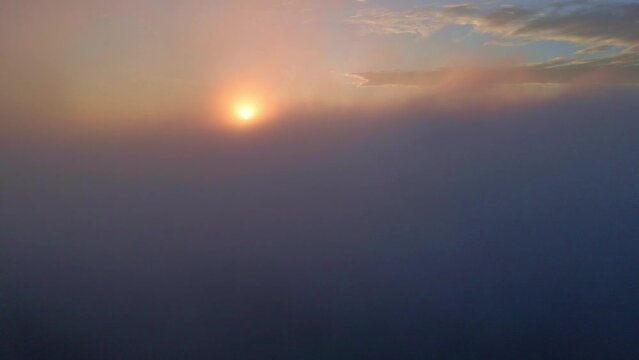 Drone camera is raising up from the thick fog to above ocean of clouds at sunrise time. View of sunrise above the endless sea of clouds. Amazing nature Cloudscape. 4K aerial view.
