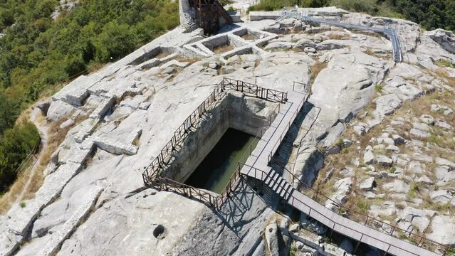 Drone orbiting and slowly retreating while showing a water reservoir enclosed with steel railings and a platform on the ancient city of Perperikon located in the province of Kardzhali in Bulgaria.