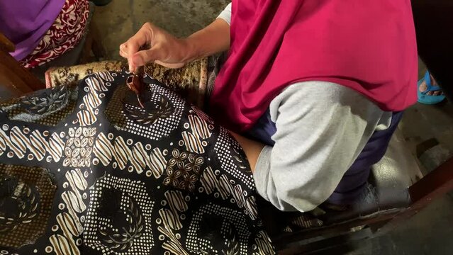 Closeup video of Indonesian old women making batik clothes. Batik is an Indonesian technique of wax-resist dyeing applied to the whole cloth