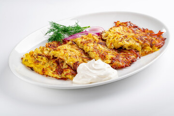 Fried Potato pancakes with sour cream in a white plate on a white background. Grated potatoes fried in oil