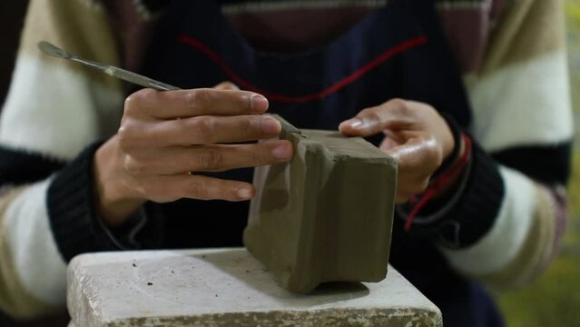 Close up over the hands of a mexican craftswoman giving details to a square shaped clay craft
