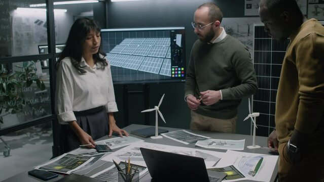 Side pull out footage of diverse team of engineers brainstorming ideas on advancing alternative energy generating technologies during office meeting