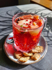 Close-up of a hot tea mug with grenadine and fruits next to cookies on a table in a cafe in bright sunlight