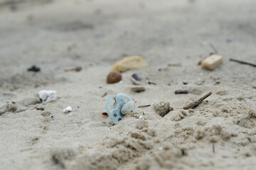 Déchets plastiques, sucette bébé et divers objets sur le sable en bord de plage. Détritus sur la plage. 