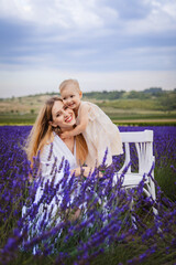 Standing on a white chair in a field of lavender, a happy mother hugs her daughter as she stands on a white chair