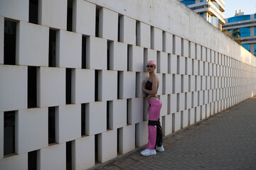 Young gay guy with pink hair and make-up and wearing pink and black dress and sunglasses is leaning on white wall making different expressions. Concept of equality and LGBTQ rights.