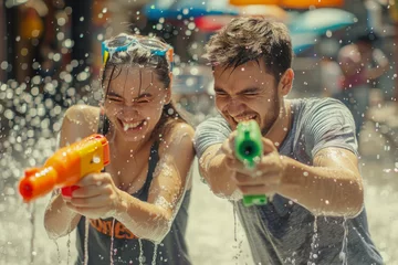 Foto op Plexiglas Happy traveler european man and woman wearing summer shirt holding colorful squirt water gun over blur city, Water festival holiday concept © grapestock