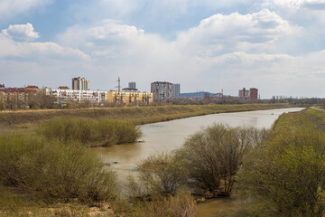City of Ussuriysk, Primorsky Krai, Russia. View of the Rakovka River flowing in the city of Ussuriysk. Residential buildings in the distance. Spring city landscape.