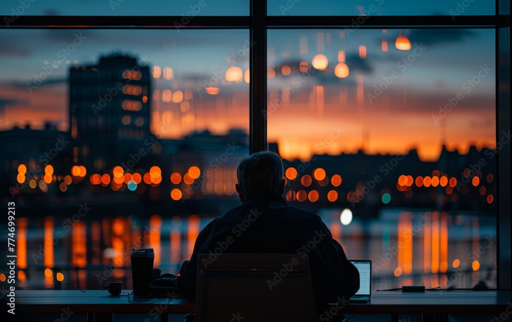 Poster a man is sitting at a desk with a laptop in front of him. the room has a window with a view of the c