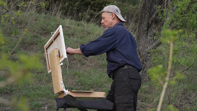 A male artist paints a landscape in oil on canvas. Nature Oil Painting