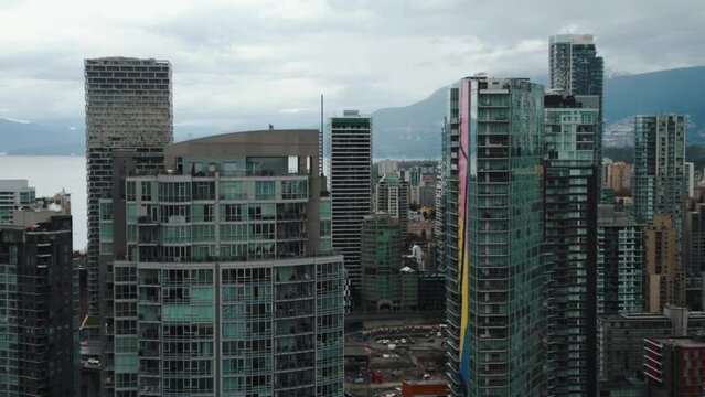 close up aerial shot going backward between buildings in Vancouver city, yaletown, with mountains and ocean in the background on an overcast day
