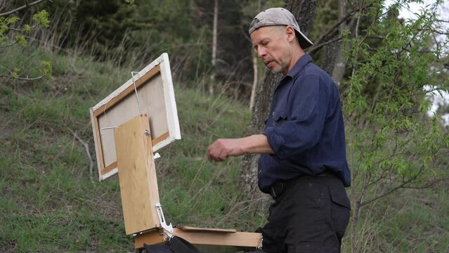 A professional male artist paints with oil paints on canvas. Plein Air Painting