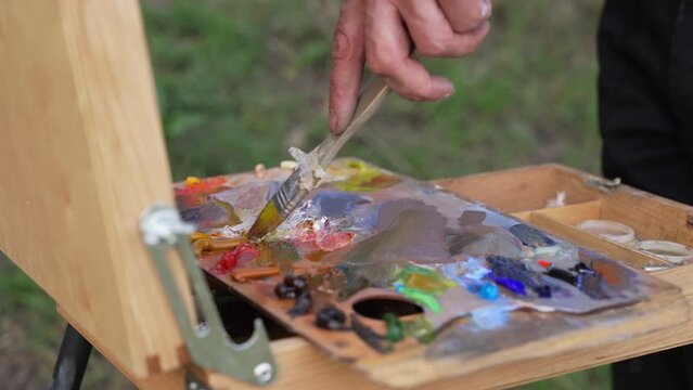 The artist mixes oil paints on the palette with a brush. Plein Air Painting