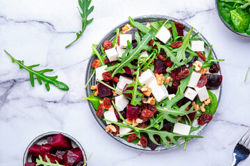 Sweet beetroot salad with feta cheese, fresh arugula, raisins and nuts, marble table background, top view