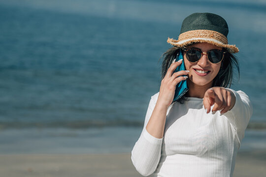 young woman talking on mobile phone on the beach and pointing a direction