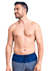 Young handsome man wearing swimwear looking away to side with smile on face, natural expression. laughing confident.