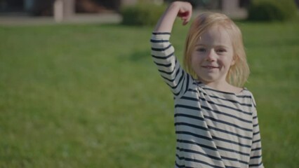 Follow me. Funny excited blonde little girl looking at camera inviting to follow her. Come here concept. Cute little girl on a sunny day on grass.