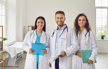Successful team of medical doctors are looking at camera and smiling while standing in hospital....