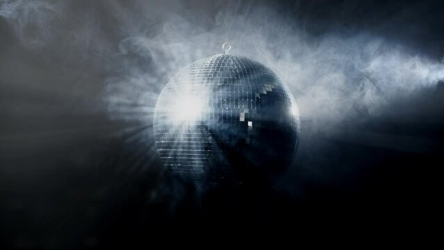 A colorful disco mirror ball illuminates the backdrop of a nightclub. The party lights up the disco ball.