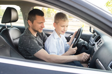 Obraz premium Dad shows his son how to drive a car. The child is driving with dad. Global Day of Parents
