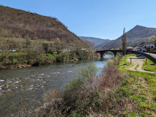 Fototapeta na wymiar Um pequeno rio serpenteando entre montanhas, ladeado por uma pitoresca ponte e uma vila envolvente num dia ensolarado
