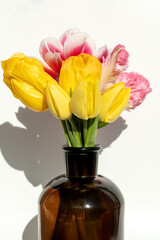 Yellow and pink tulips in brown glass bottle on white background.