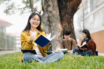 Obraz premium Asian Students are studying the campus park. Young people are spending time together. Reading book, working with laptop and tablet