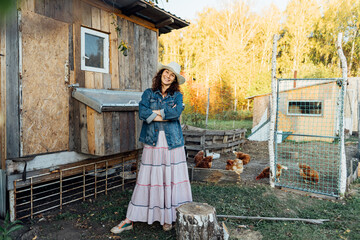Joyful Woman against the background of a chicken coop with chickens in the backyard of a country house. Portrait of a smiling farmer at the chicken coop, a happy moment of rural life